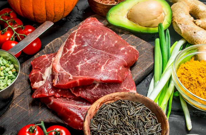 Surowa wołowina na desce w otoczeniu warzyw, przypraw i awokado