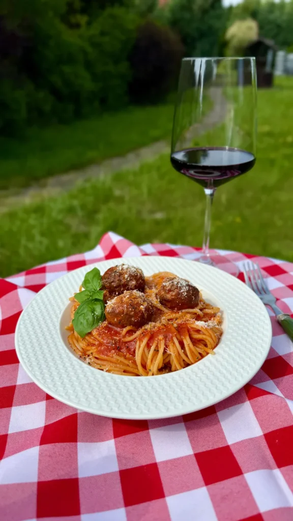 Makaron z klopsikami wege i czerwonym winem na obrusie w kratę na świeżym powietrzu