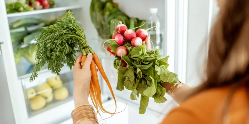 Kobieta trzymająca świeże warzywa przed lodówką