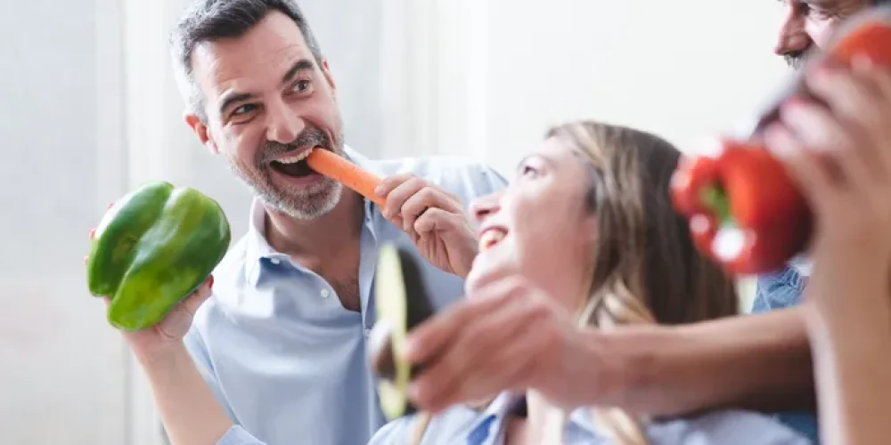 Grupa uśmiechniętych przyjaciół trzymających świeże warzywa i jedzących marchewkę
