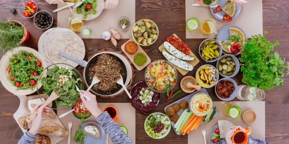 Stół pełen warzywnych potraw, przy którym siedzą przyjaciele